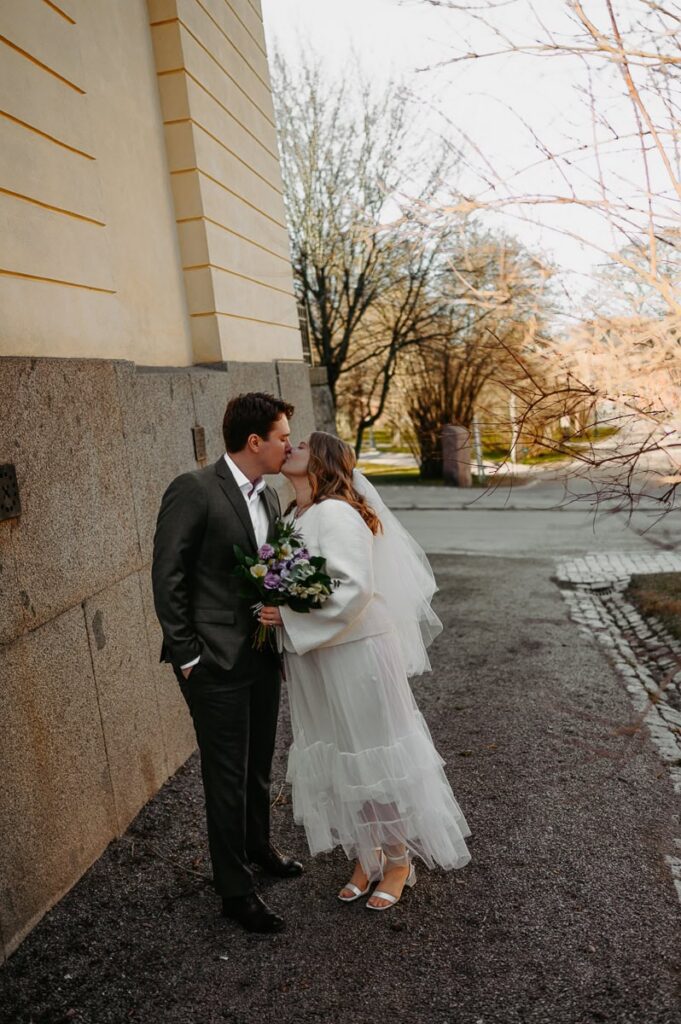 Brudpar kysser varandra vid en husvägg.