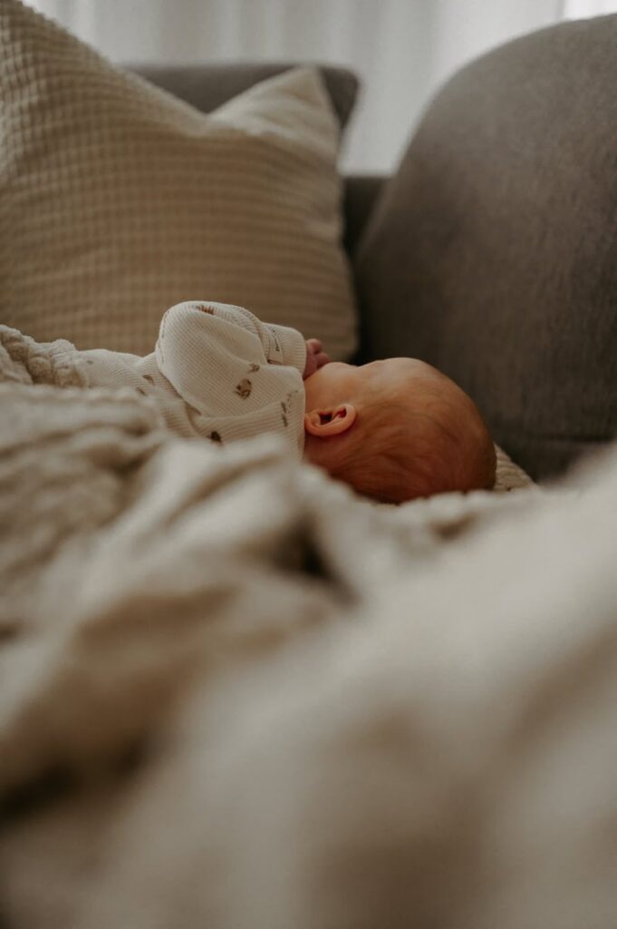 Bebis ligger på soffa och suger på sina händer under en filt.