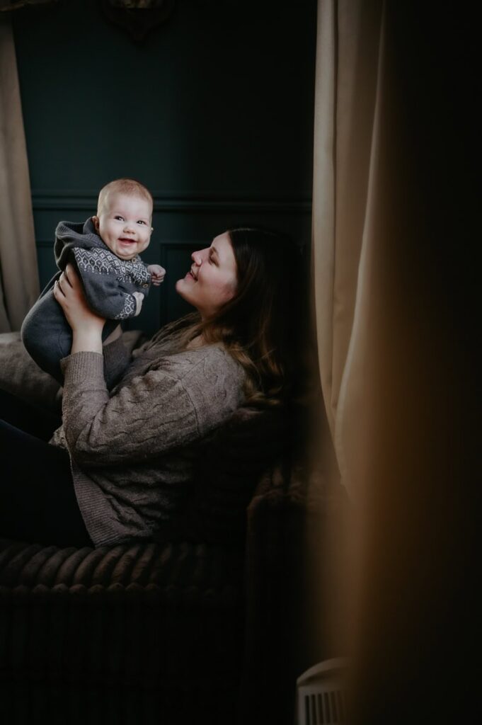 Bebis står i sin mammas knä och ler mot kameran.