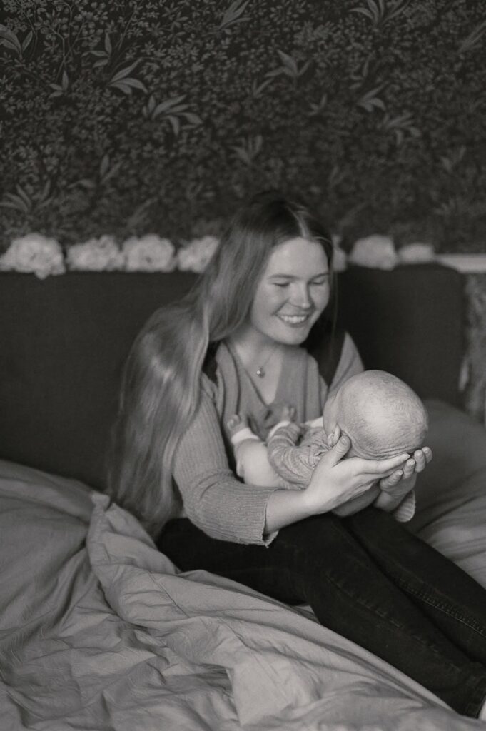 Mamman håller sin bebis i knät och ler mot han.