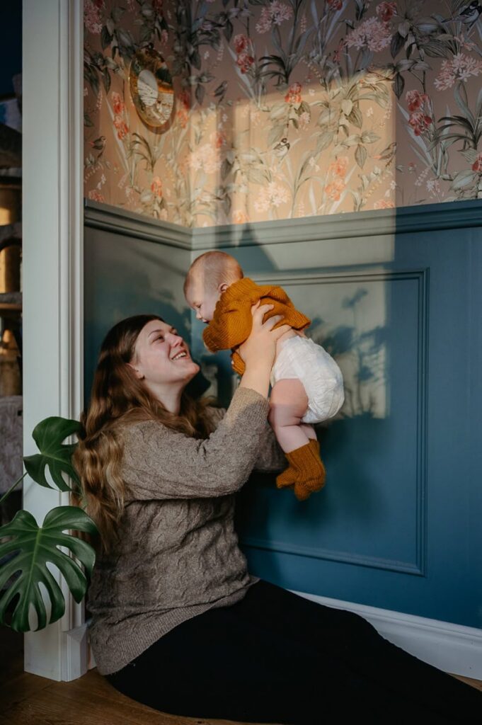 Mamman och bebisen sitter på golvet med solen som lyser i på dem och ger fina skuggor på henne och bebisen.