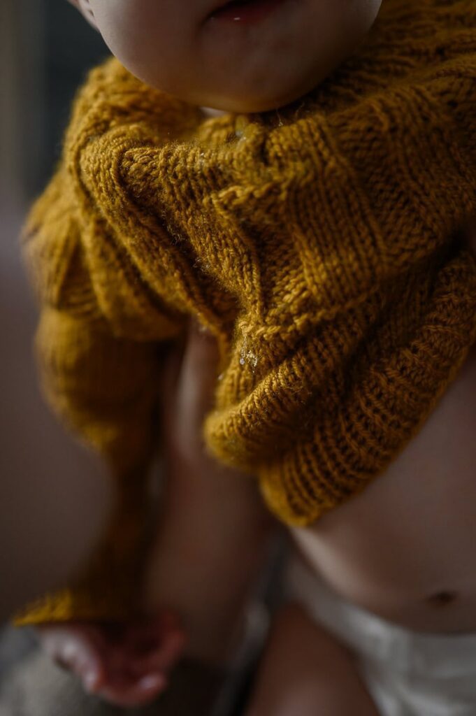 Närbild på vacker stickad tröja i senapsgult med en liten dräggel droppe på.
