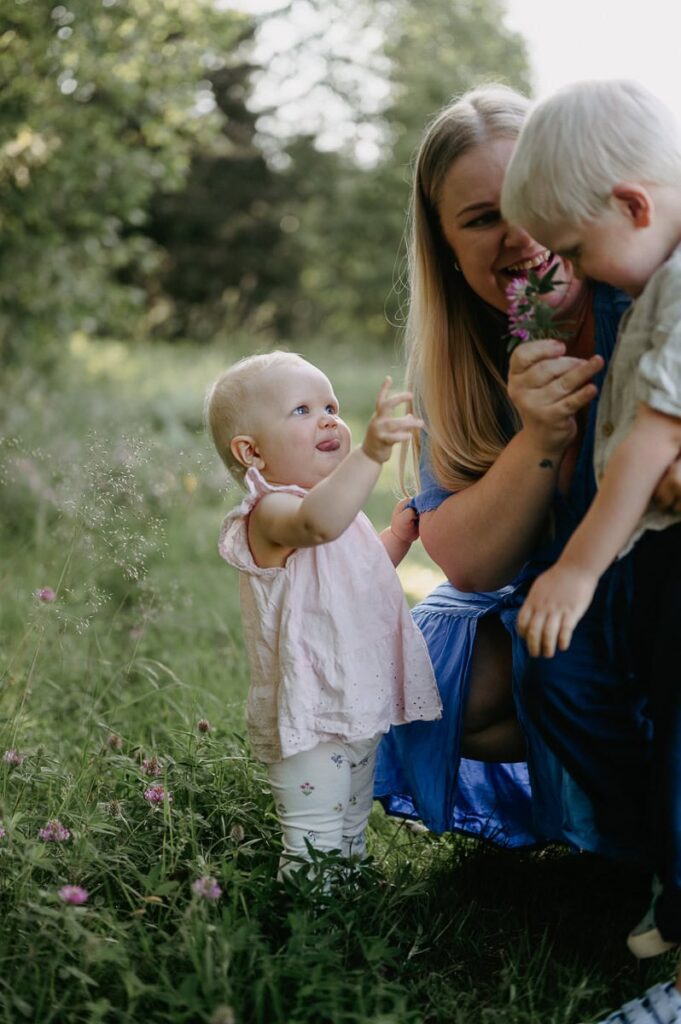 Mamma och två barn leker med en blomma i sommarkvällen.