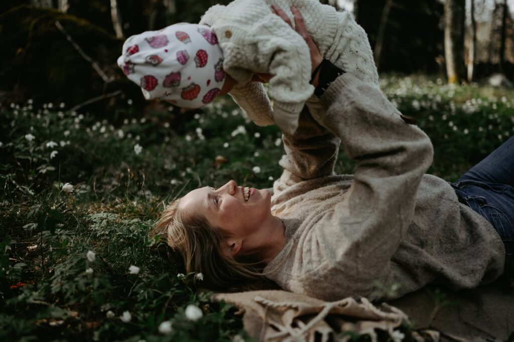 Mamma håller upp sin bebis i sina armar när hon ligger i gräset.